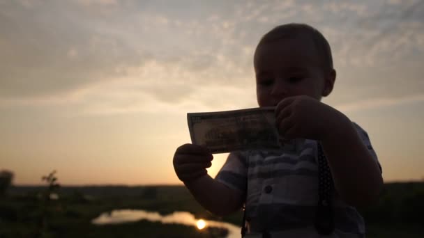 Een schattige kleine jongen kijkt met belangstelling op een honderd dollar Bill in slow motion — Stockvideo