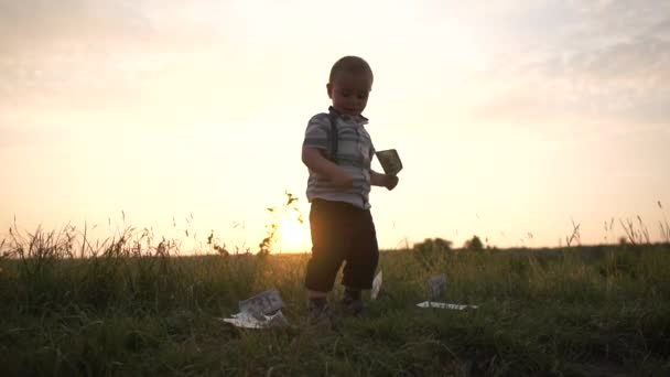 Un niño alegre levanta billetes de un dólar de la hierba y lo lanza en cámara lenta — Vídeos de Stock