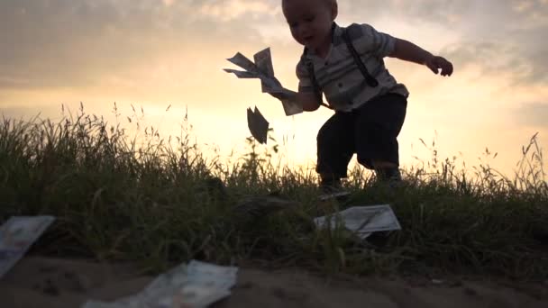 Malý chlapec šťastně hází na zem obrovskou hromádku dolarových bankovek, pomalý pohyb — Stock video
