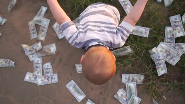 小さな子供がスローモーションで彼の周りに100ドル紙幣を投げる — ストック動画