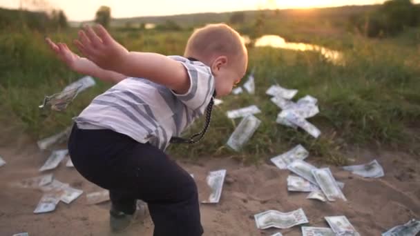 Milý chlapec šťastně hází na zem obrovskou hromádku dolarových bankovek, pomalý pohyb — Stock video