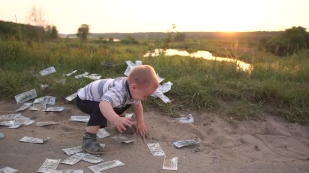 Der Junge springt fröhlich im Sonnenuntergang um das verstreute Geld herum — Stockvideo