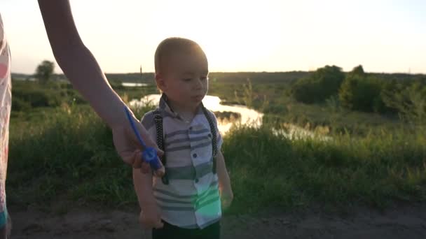 A joyful small boy waving a bubble wand on the field in slow motion — Stock Video
