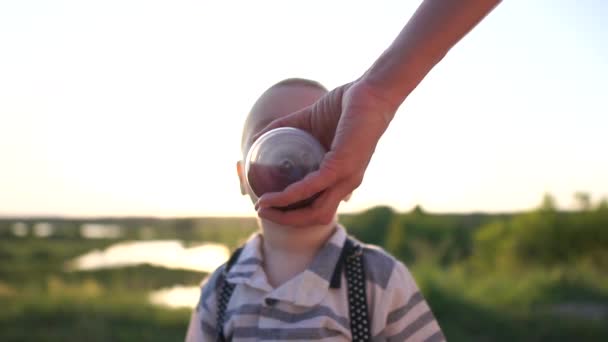 Malý hoch pije z dětské láhve, kterou maminka drží při západu slunce v pomalém pohybu — Stock video