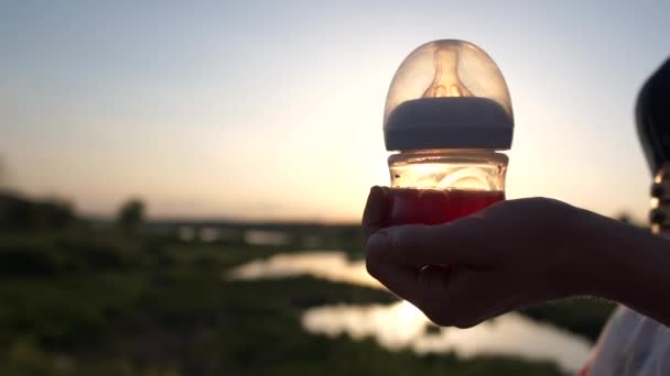 Een meisje houdt een baby fles met compote op de achtergrond van een natuur bij zonsondergang — Stockvideo