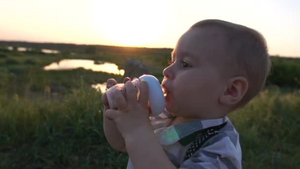 Um menino bonito bebe uma compota de uma mamadeira ao ar livre em câmera lenta — Vídeo de Stock