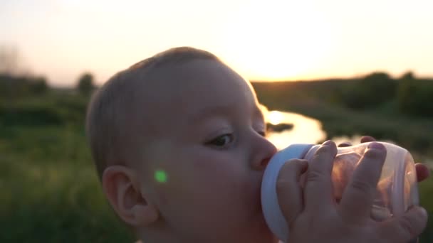 Маленький мальчик пьет напиток из детской бутылочки в поле в замедленной съемке — стоковое видео