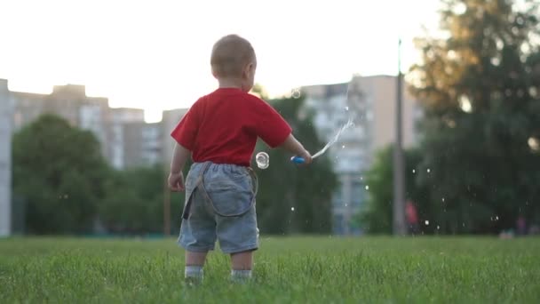 A small blond boy jumps and happily waving his wand with soap bubbles — Stock Video