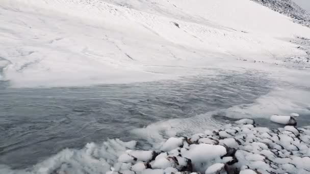 River with melting streams moving between snowy banks in mountains in slo-mo — Stock Video