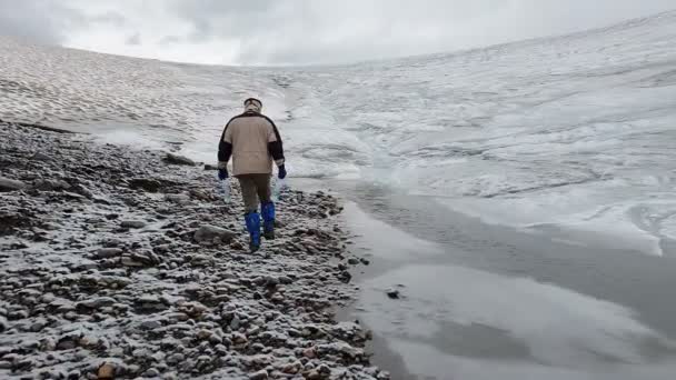 Hermoso arroyo que corre en las montañas nevadas y turista va en slo-mo — Vídeos de Stock