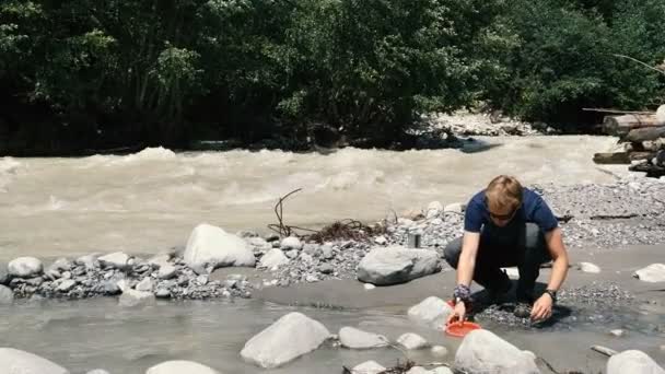 Un joven turista sentado y tomando agua de un río en Georgia en slo-mo — Vídeos de Stock