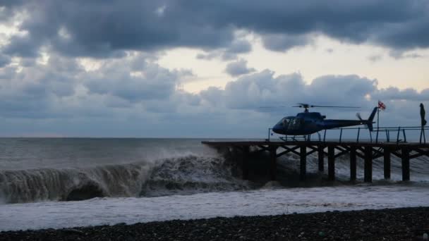 Gestroomlijnde helikopter staande op een pier in de stormachtige Zwarte Zee-kust — Stockvideo