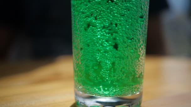 Éclaboussures de cola vert avec des bulles dans un verre debout sur une table au ralenti — Video