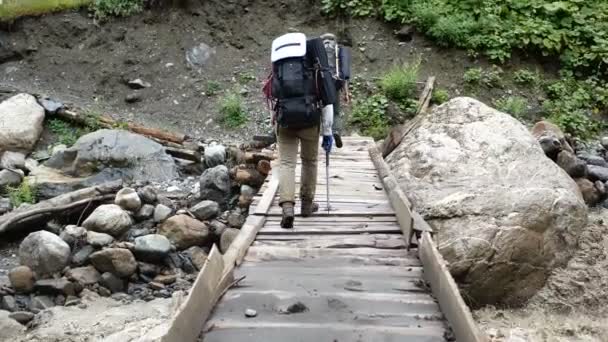 Dois jovens alpinistas vão em uma ponte de madeira nas montanhas georgianas em slo-mo — Vídeo de Stock