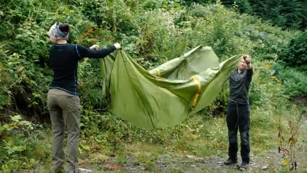 Två glada turister skakar på sitt tält i georgiska berg på sommaren — Stockvideo