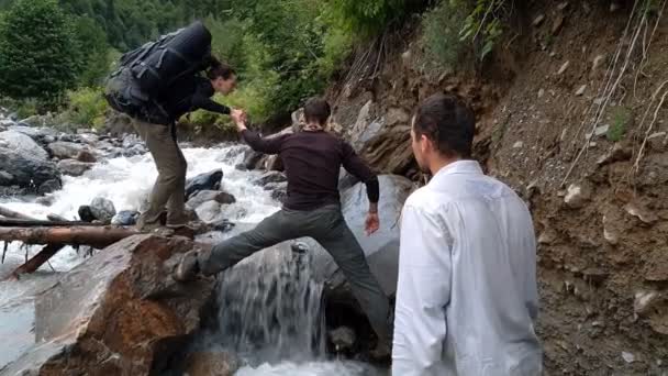 Chica alegre ayudando a un hombre a mantener las piernas como un arco sobre una cascada de montaña — Vídeos de Stock