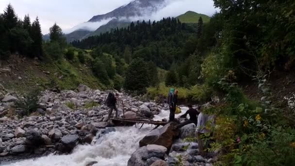 Четыре туриста пересекают небольшой деревянный мост через горный поток — стоковое видео