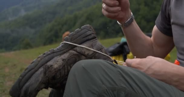 Jovem sentado e consertando uma sola de inicialização com uma corda em montanhas em slo-mo — Vídeo de Stock