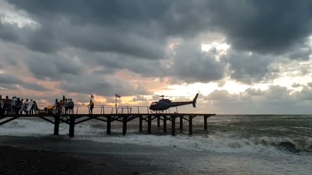 Helicóptero con cuchillas giratorias en el muelle con gente en la costa tormentosa en slo-mo — Vídeo de stock