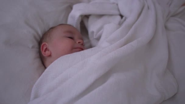 Малыш сладко спит на большой кровати с белым бельем в замедленной съемке — стоковое видео
