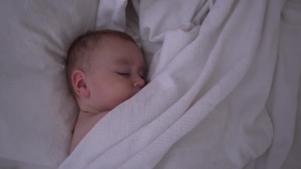 Un bambino sveglio addormentato sdraiato sotto una coperta bianca al rallentatore — Video Stock