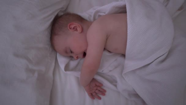 小さな赤ちゃんを甘くあくびをして、白いリネン、スローモーションで大きなベッドであくびをした — ストック動画
