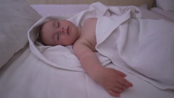Однорічна дитина солодко спить на спині на великому ліжку, повільний рух — стокове відео