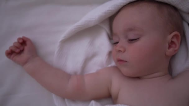 A cute baby sleeps on the big bed with white linens, slow motion — Stock Video