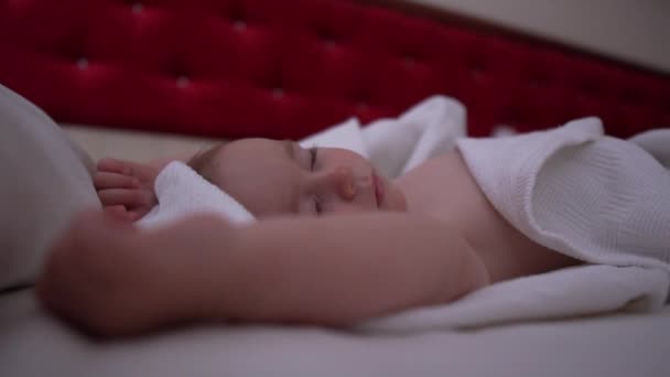 Un piccolo bambino nudo dorme con le mani alzate su un grande letto rosso al rallentatore — Video Stock