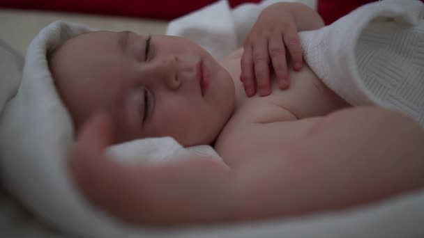 Een mooie baby slaapt zoet op een groot bed onder een witte deken in slow motion — Stockvideo