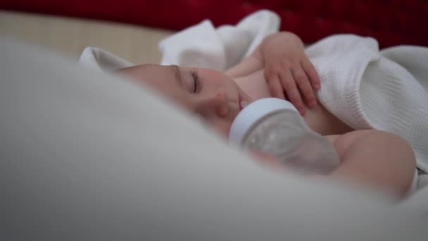 A sleeping baby with bottle is lying on the bed with white bedding, slow motion — Stock Video