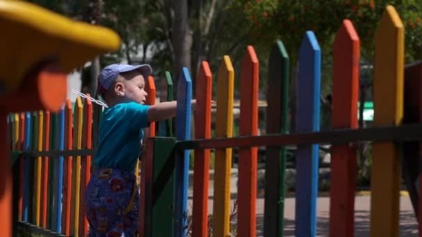 Mały chłopiec przebywa w pobliżu colorfulrainbow ogrodzenia w zwolnionym tempie — Wideo stockowe