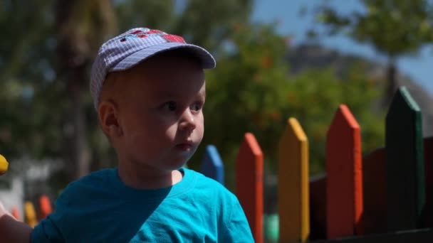 Маленький милий хлопчик пішов до кольорового дерев'яного паркану, повільний рух — стокове відео
