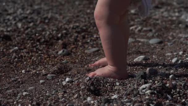 Las piernas de un niño pequeño en la playa en la arena con conchas, cámara lenta — Vídeos de Stock