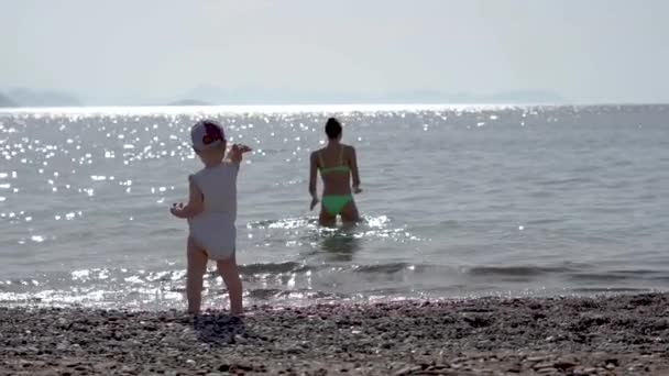 En liten pojke kastar en sten i havet, flickan simmar i havet, slow motion — Stockvideo