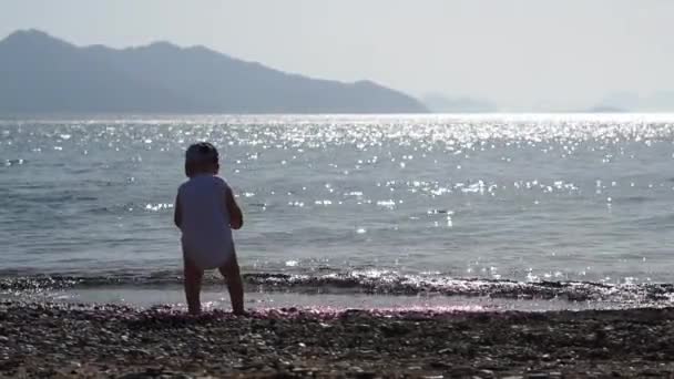 Bir çocuk güneşten parlak deniz suyuna bir çakıl taşı atar, yavaş hareket — Stok video