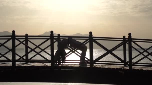 Holka dělá jómu na mostě proti moři při východu slunce v pomalém pohybu — Stock video