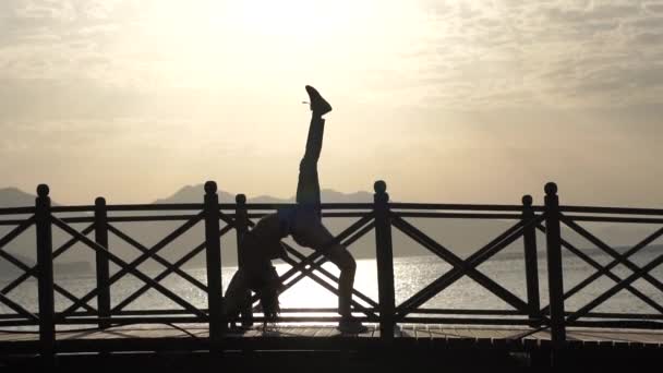 해질 녘에 바다 근처에서 다리를 들고 다리를 포즈를 취하는 다리 포즈를 취한 소녀의 실루엣 — 비디오