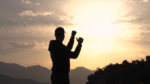 Молодий хлопець показує жест гаразд стоячи збоку на заході сонця в повільному русі — стокове відео
