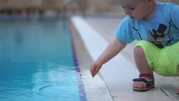 Маленький симпатичный малыш с интересом прикасается к воде бассейна в замедленном режиме — стоковое видео