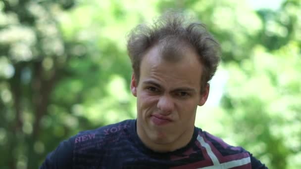 Verwirrter junger Mann mit lustiger Fratze, der in einer grünen Gasse in Slo-mo steht — Stockvideo