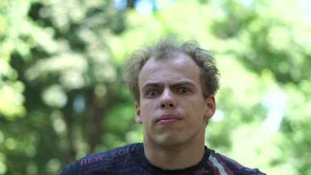 Förbryllad ung man med ett lidande grimas stående i en grön gränd i slo-mo — Stockvideo