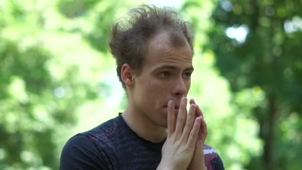 Gondolkodó fiatalember egy vicces arc dobolás ujjaival az állán a parkban slo-Mo — Stock videók