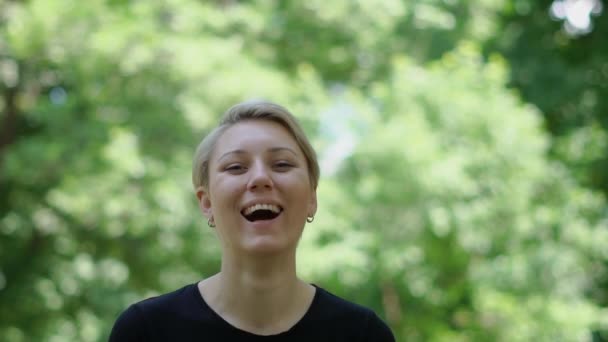 Neşeli sarışın kadın gülümseyen ve slo-mo yaz aylarında yeşil bir parkta gülüyor — Stok video