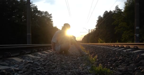 4K-facet wznosi się z ziemi wśród torów kolejowych o zachodzie słońca, w zwolnionym tempie — Wideo stockowe