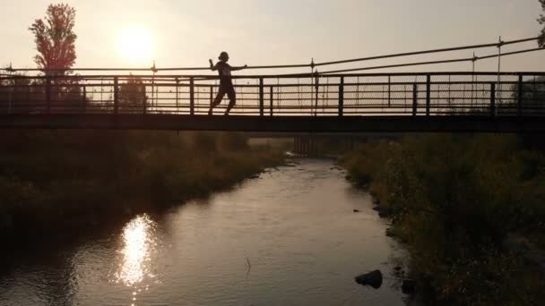 Male silhouette dancing contempt on a pedestrian bridge at sunset — Stock Video