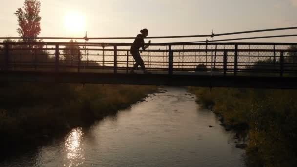 Joven silueta bailando disco en un puente estrecho al atardecer — Vídeos de Stock