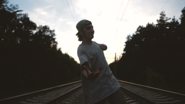 一个男孩在日落时分在铁轨附近用手做一个很酷的动作，慢动作 — 图库视频影像