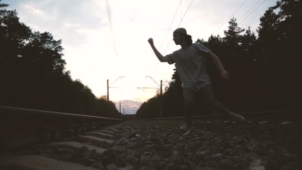 Een kerel danst Krump, maakt een coole beweging met de hand in de buurt van het spoor bij zonsondergang, Slow Motion — Stockvideo