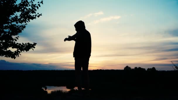 Silhouette of a guy in a hooded sweater, pointing at something in nature — Stock Video